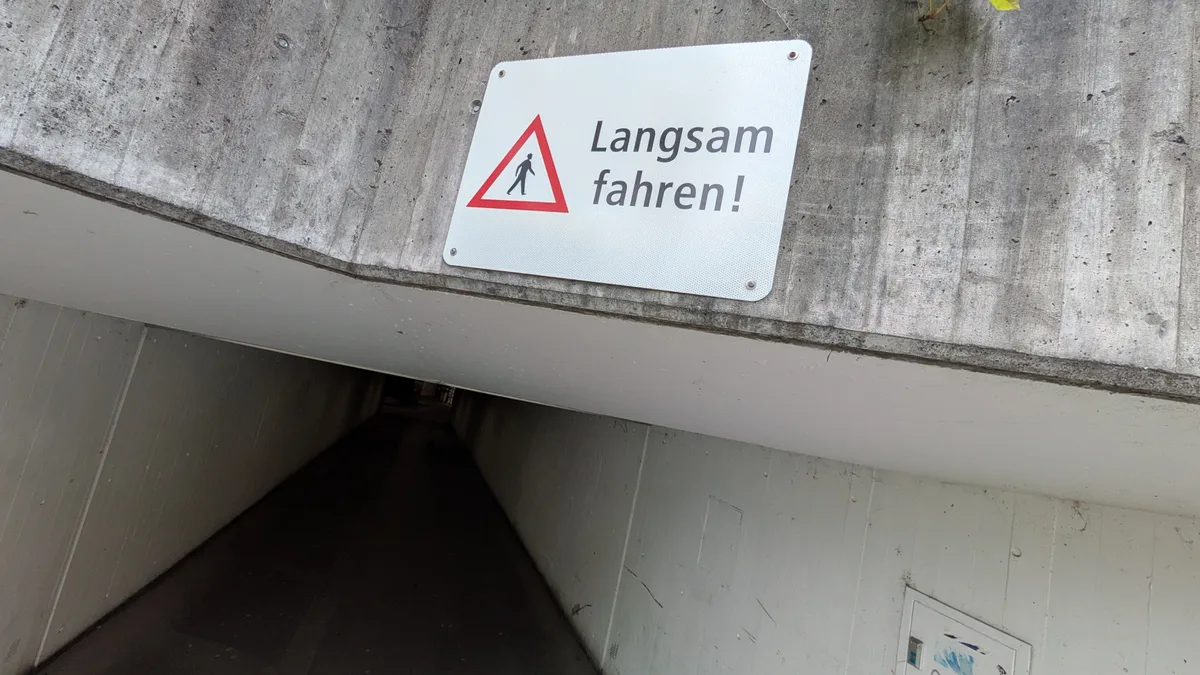 Man sieht eine düstere Bahnhofunterführung mit Passanten und Velofahrern.
